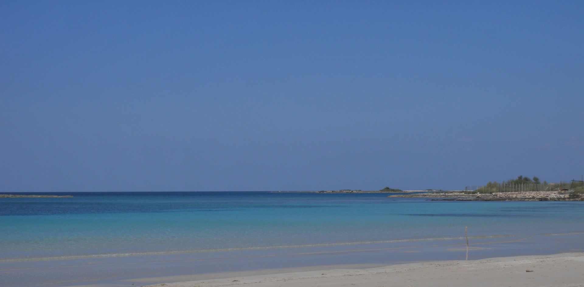 Scena di spiaggia con cielo azzurro e limpido, acqua turchese e riva sabbiosa.