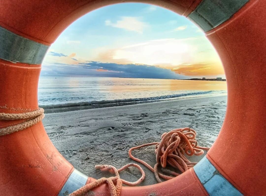 Salvagente su spiaggia sabbiosa, con vista sul mare e sul tramonto.