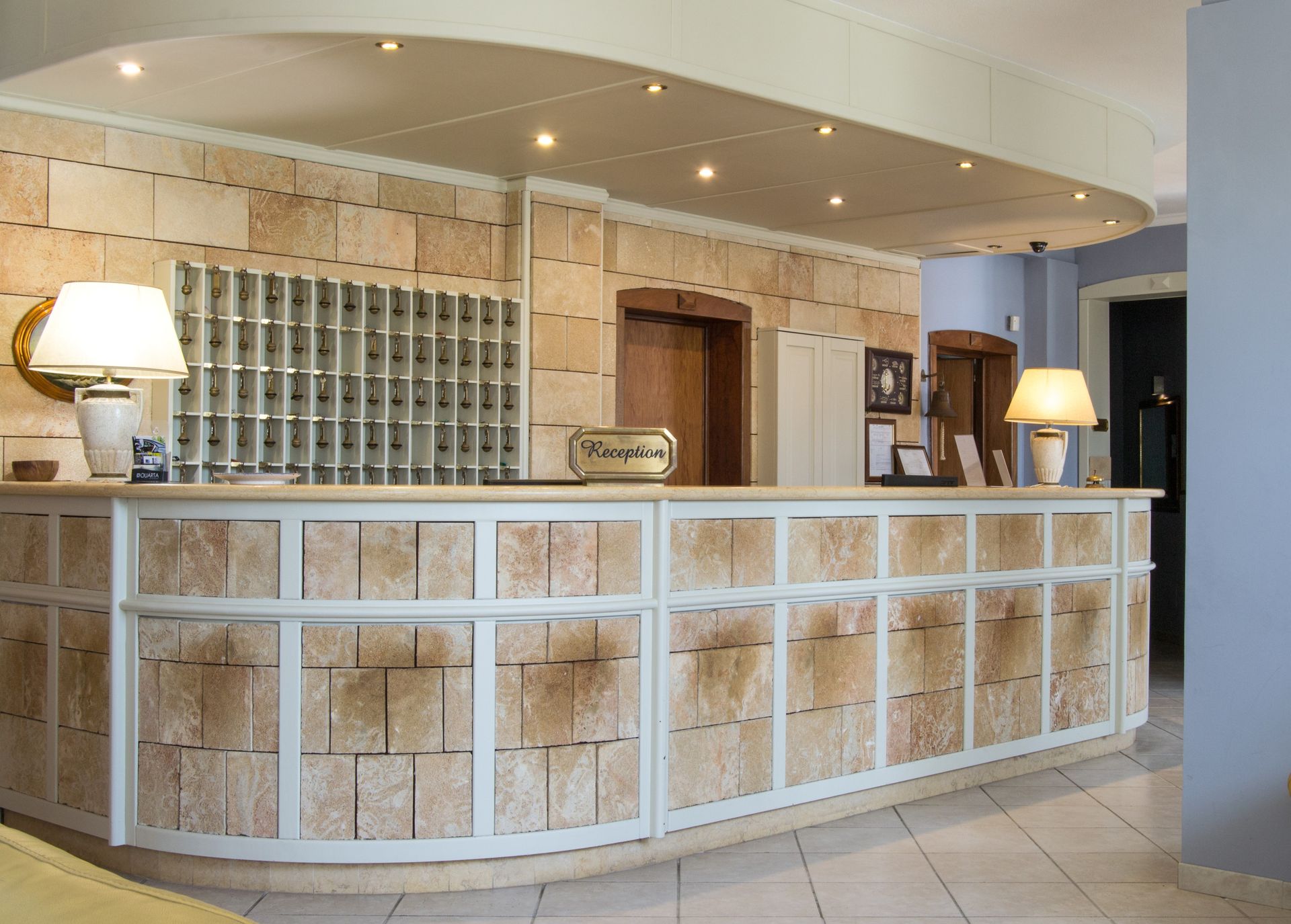 Banco della reception dell'hotel con blocchi di pietra beige, fessure per le chiavi e lampade.