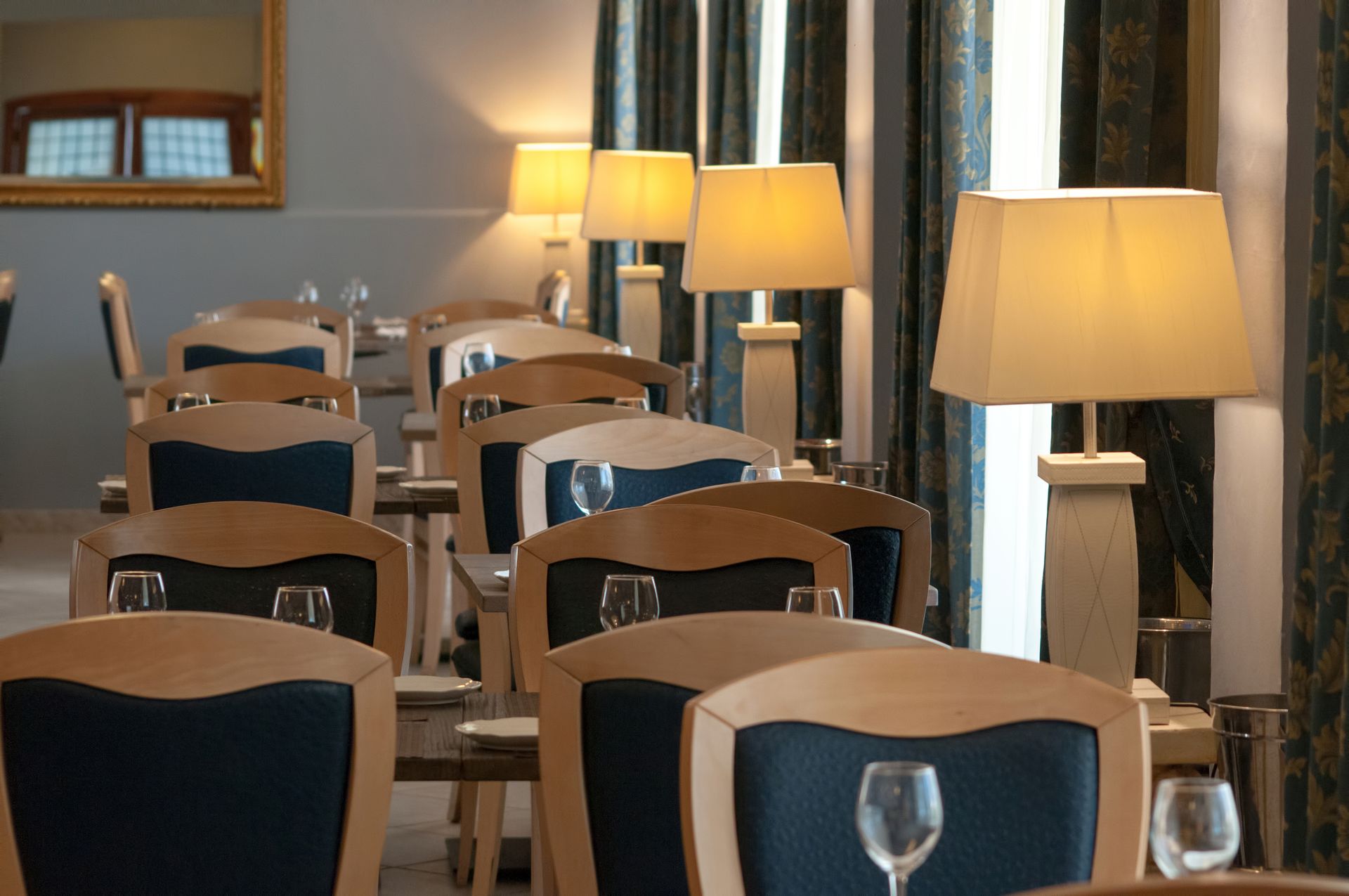 Sala da pranzo con sedie in legno, schienali blu, lampade e finestre.