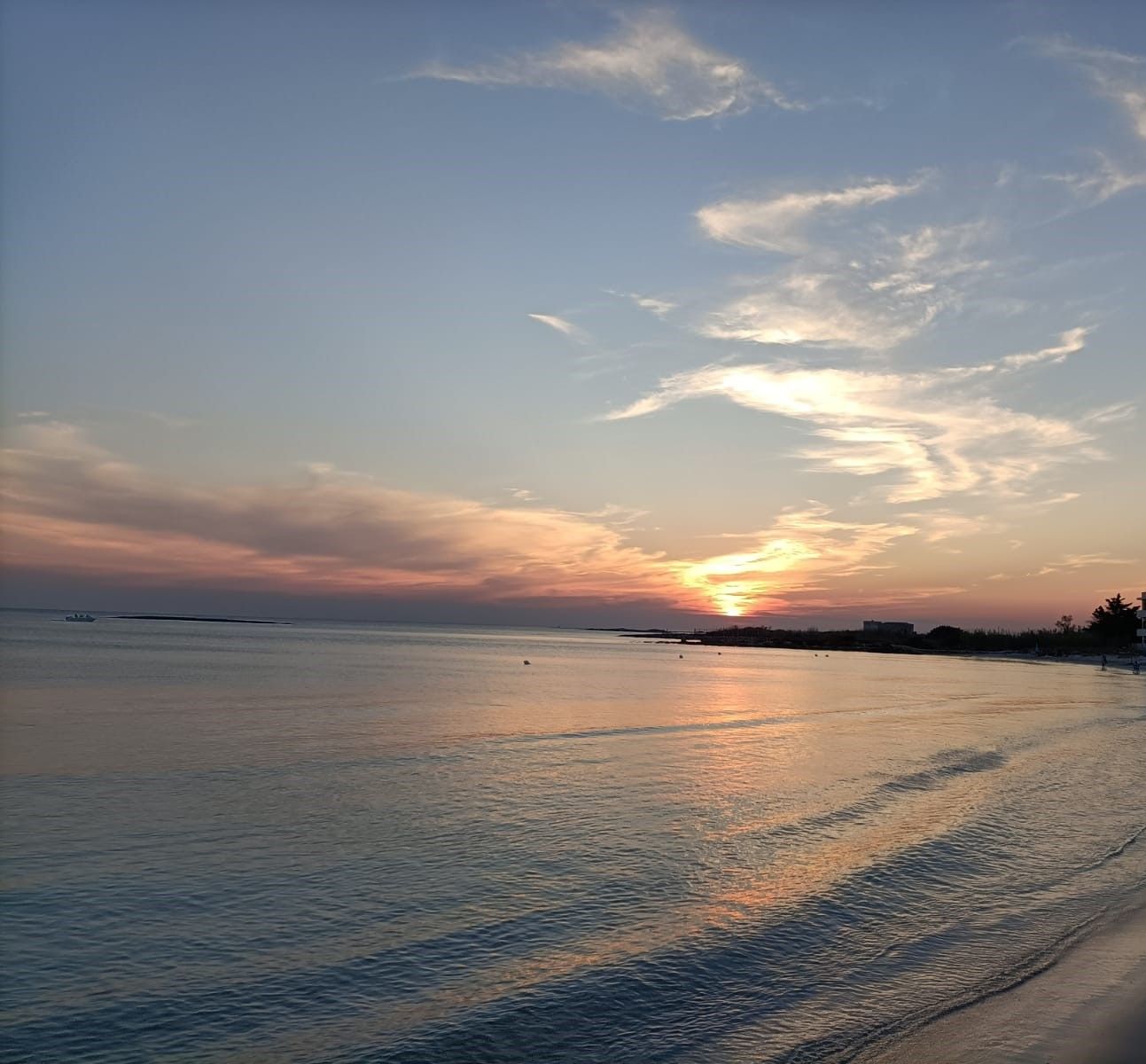 Tramonto sul mare con onde dolci; sfumature arancioni e rosa nel cielo che si riflettono sull'acqua.