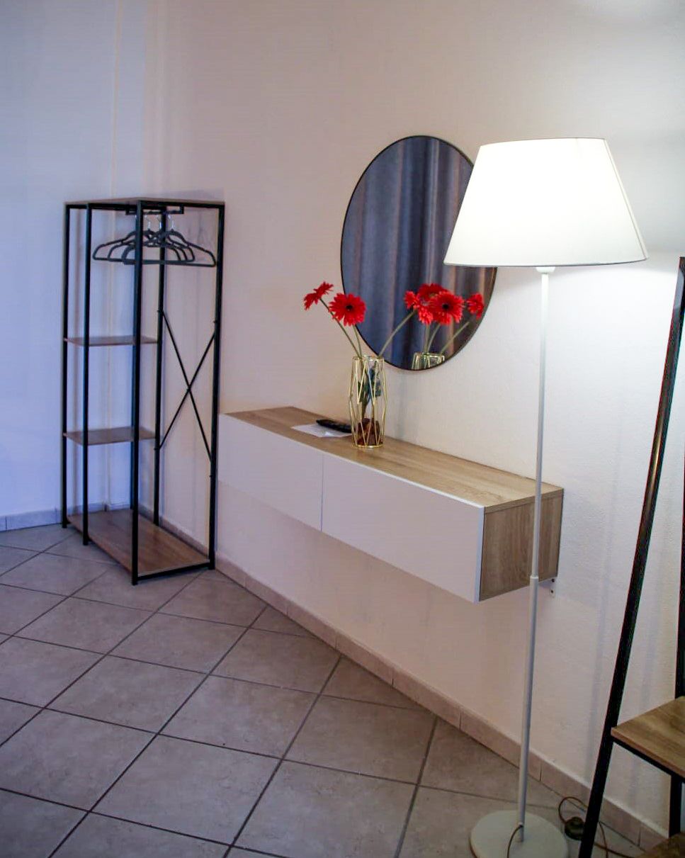 Modern room interior: coat rack, floating console with mirror and flowers, floor lamp.