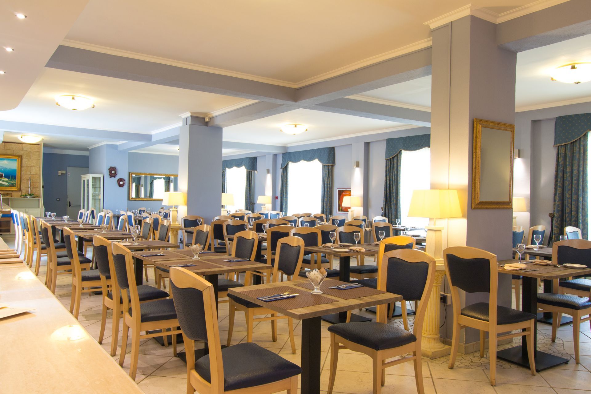 Interno del ristorante con tavoli e sedie apparecchiati per cenare; pareti e finiture di colore azzurro chiaro.