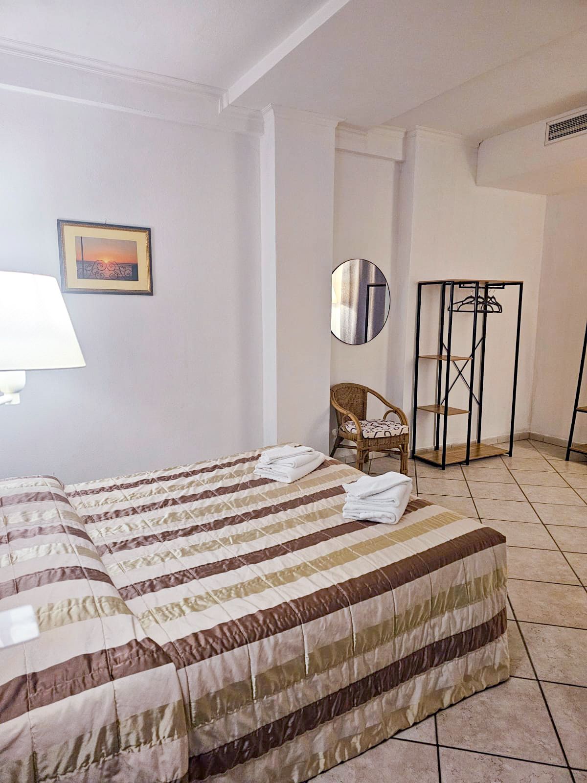 Bedroom with twin beds, striped comforters, a small chair, and a decorative mirror.