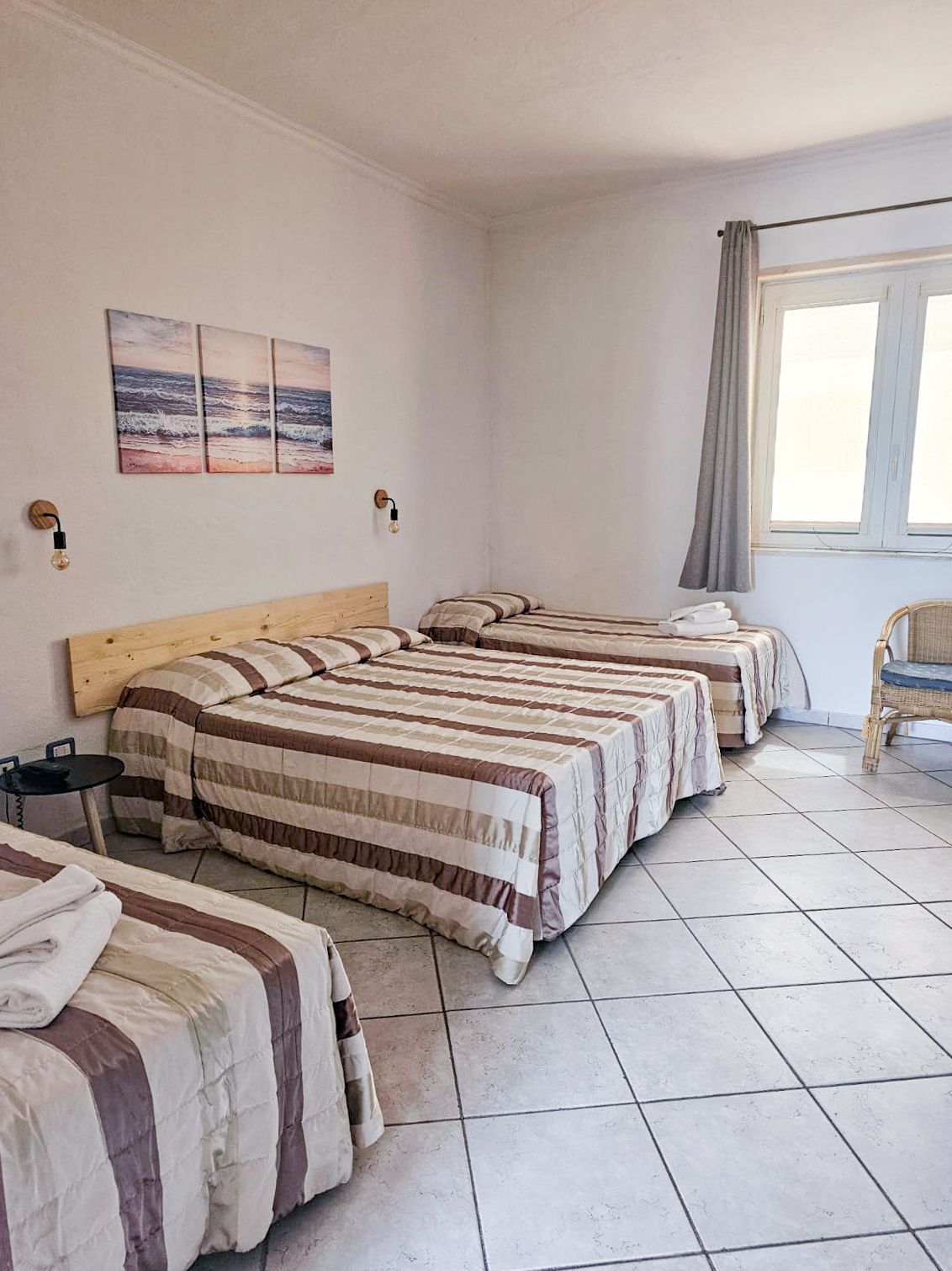 A simple room with three beds with striped bedding and a small window.