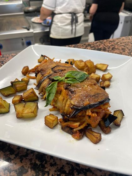 Pollo arrosto con patate a cubetti e basilico su un tavolo bianco nella cucina di un ristorante.