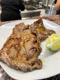 Bistecca alla griglia su un piatto bianco con uno spicchio di lime, servita in un ambiente da cucina.
