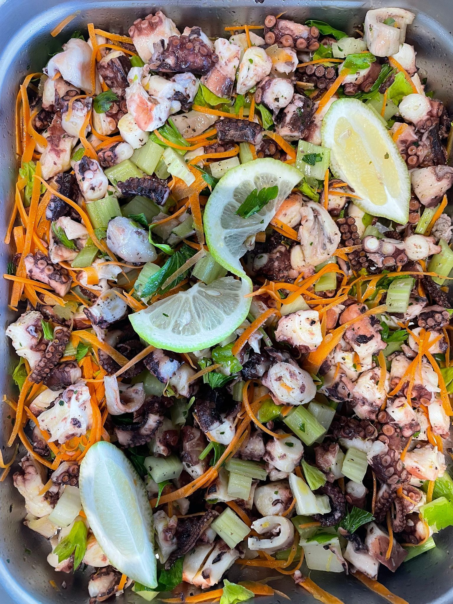 Vassoio di frutti di mare arrostiti guarnito con spicchi di limone, erbe aromatiche e verdure tritate.