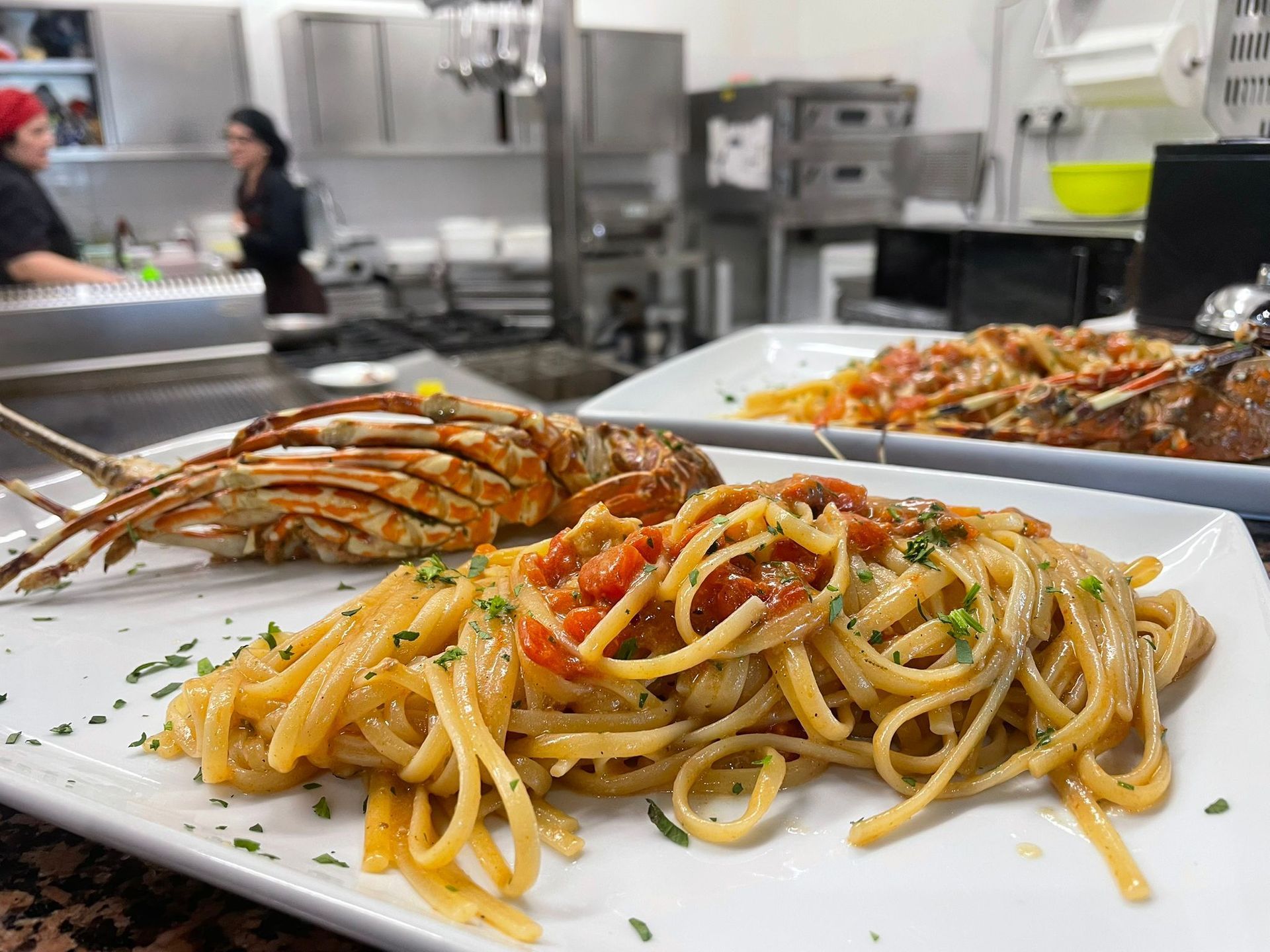 Piatto di pasta con aragosta servito in una cucina di ristorante con attrezzature in acciaio inox.