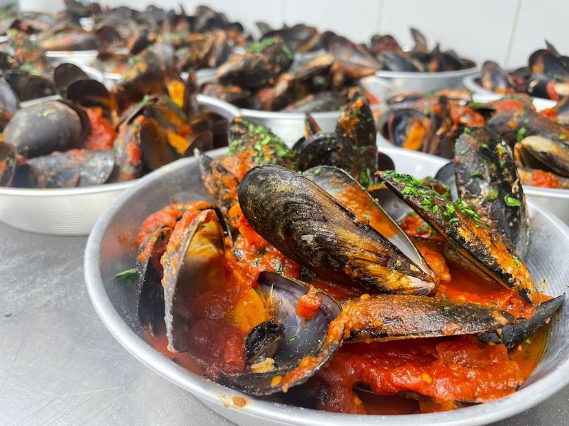 Piatti di cozze in salsa rossa, guarnite con erbe aromatiche, serviti al tavolo di un ristorante.