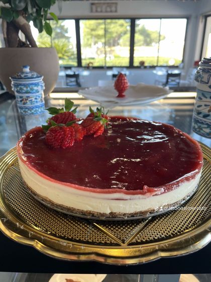 Cheesecake con lamponi su un piatto d'oro accanto a una finestra soleggiata
