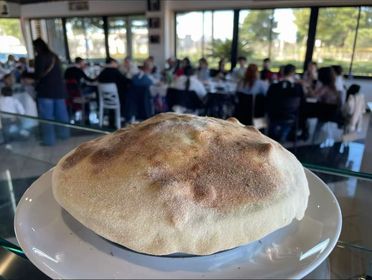 Una pagnotta rotonda su un piatto bianco in un caffè, con persone sedute sullo sfondo.