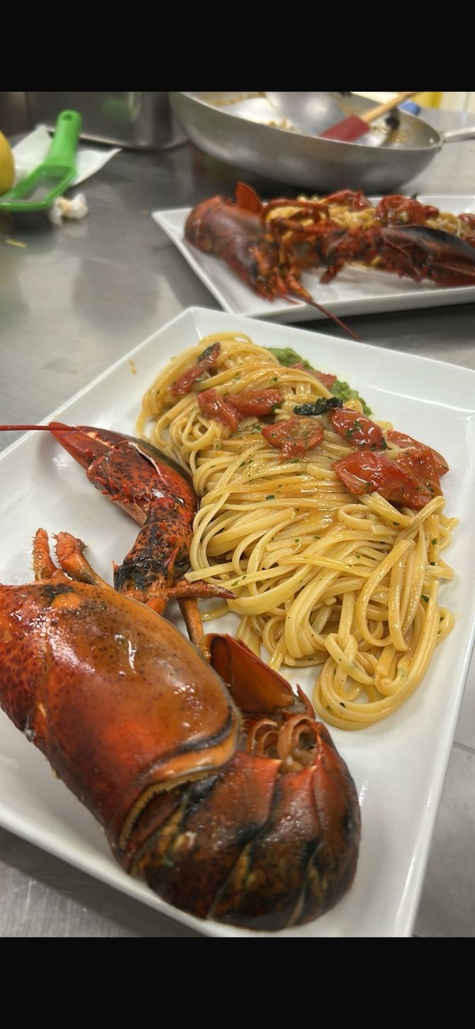 Piatto con spaghetti al sugo di pomodoro e due mezze aragoste grigliate su un tavolo in acciaio inox.