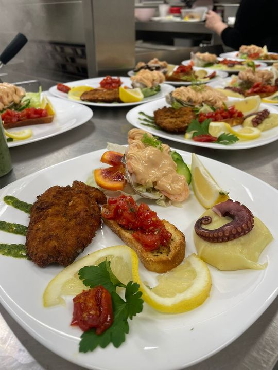 Antipasti gourmet impiattati con guarnizioni su un bancone della cucina, pronti per essere serviti.