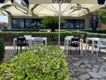 Tavolini da caffè all'aperto con tavoli e sedie in bianco e nero sotto grandi ombrelloni, accanto a una siepe e un sentiero in pietra.