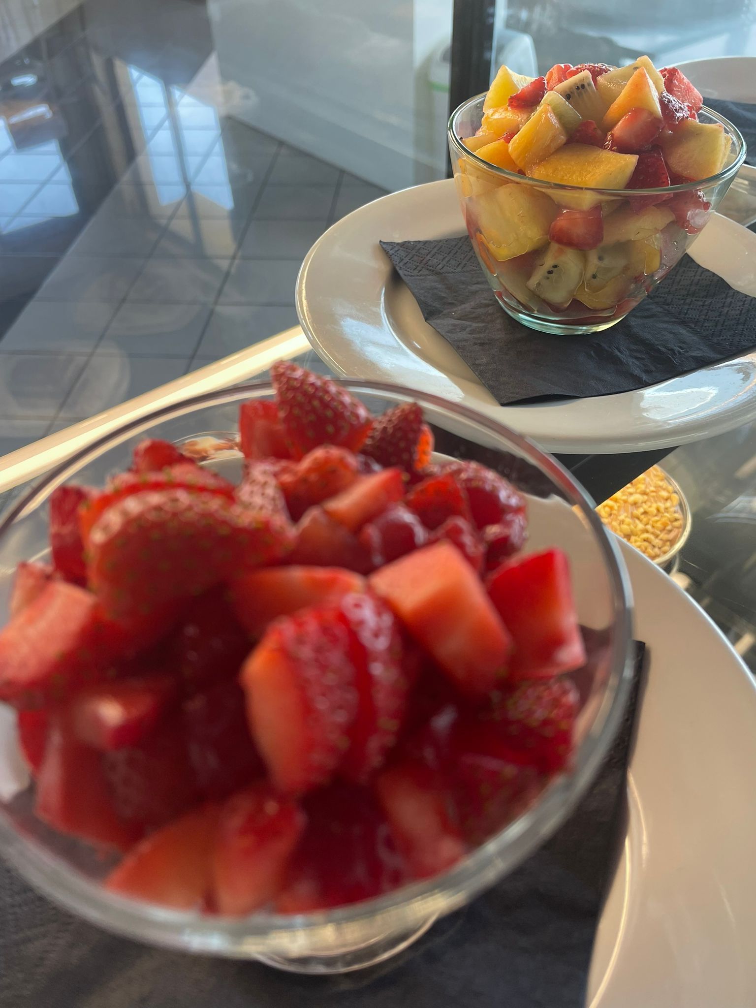 Due ciotole di dessert alla frutta fresca su un vassoio, una guarnita con fragole e l'altra con macedonia di frutta mista.