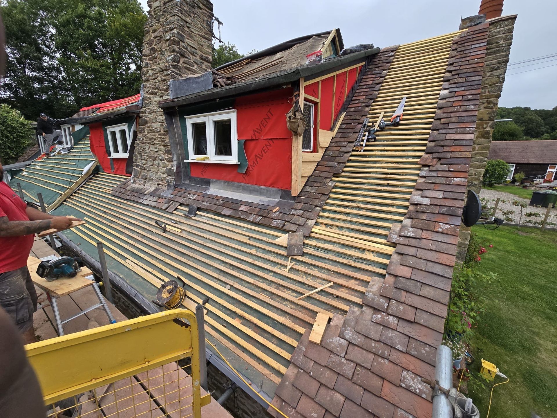 A man is working on the roof of a red house.