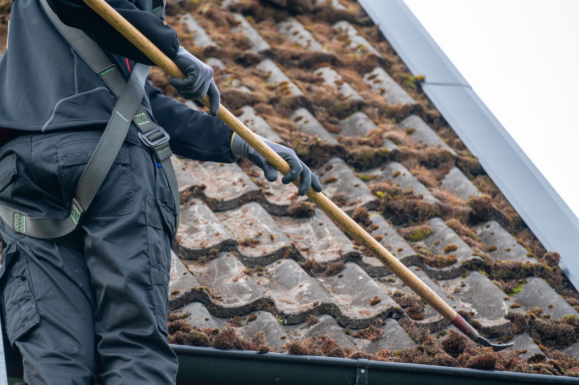 A man is cleaning a roof with a rake.