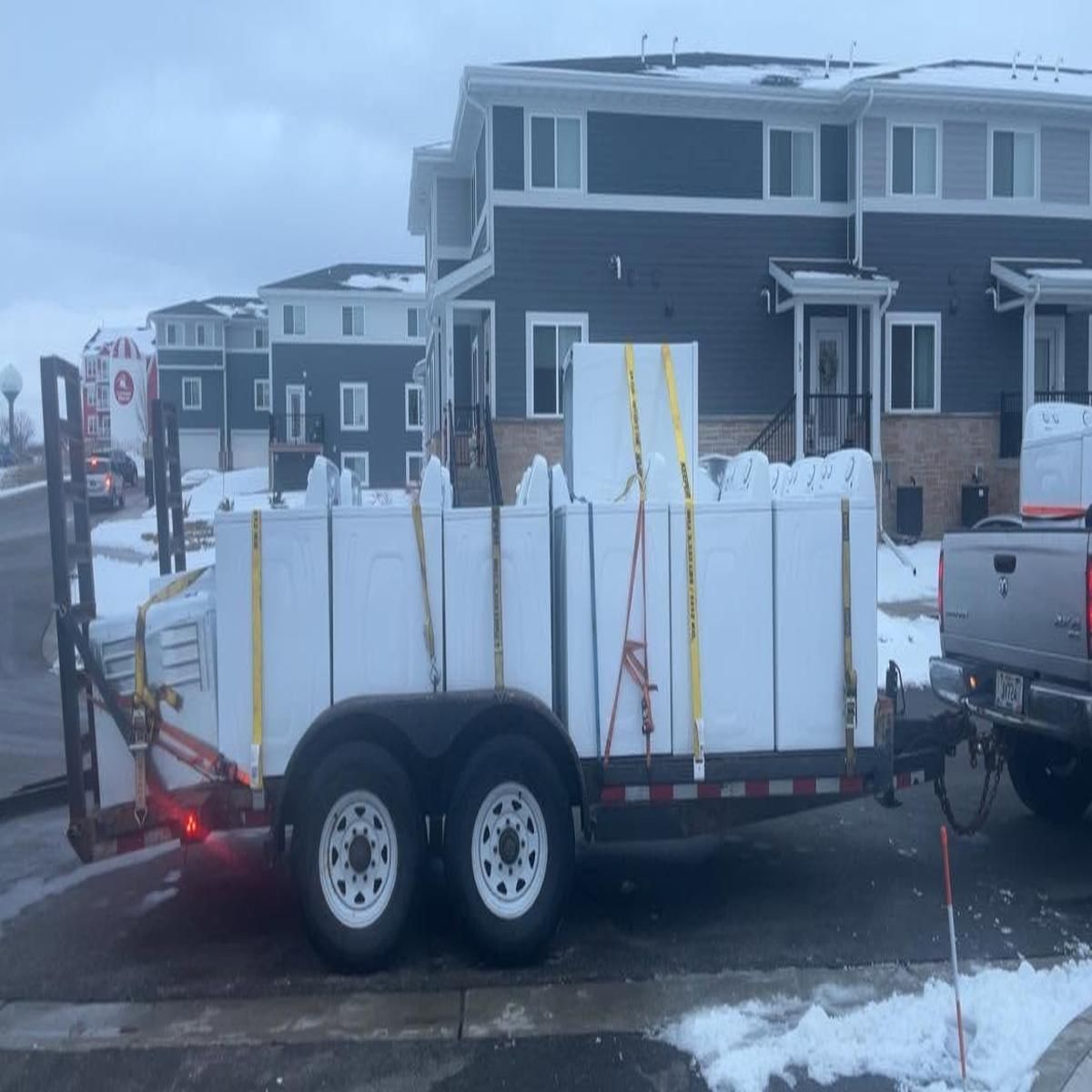Trailer loaded with white panels and straps parked on a snowy residential street.