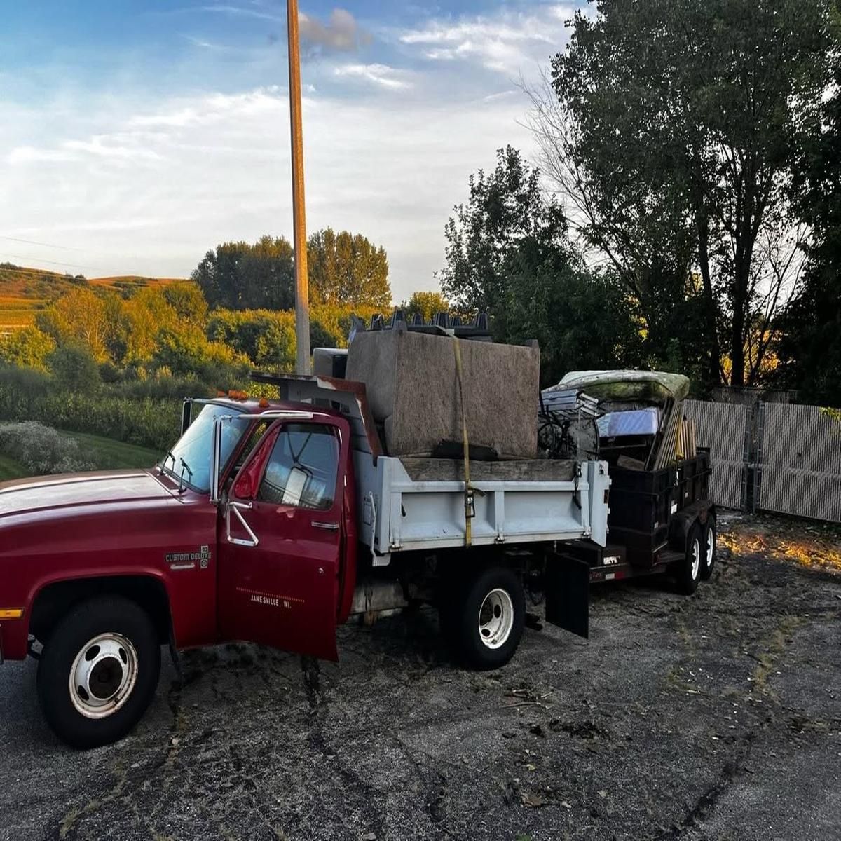 Red pickup truck with a white dump bed and large stone load parked on a gravel lot at sunset.