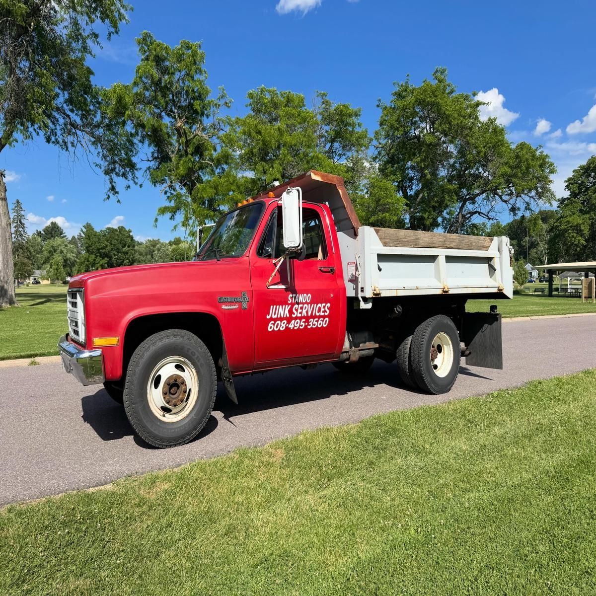 Red dump truck parked on a road beside a grassy park under a blue sky