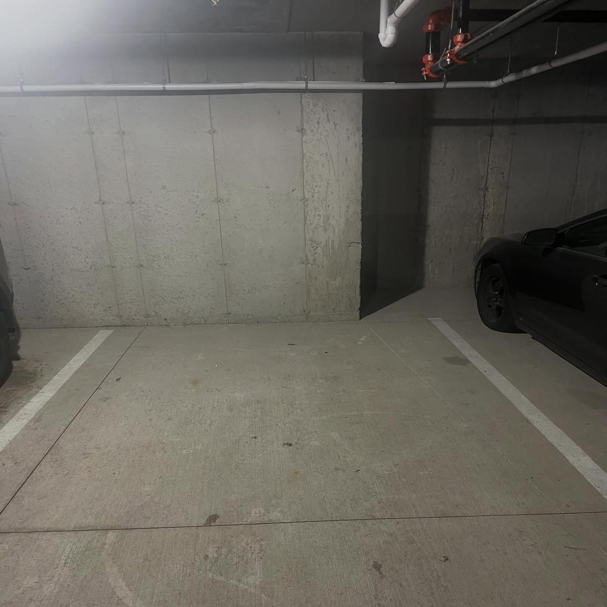 Empty concrete parking garage space with a black car parked on the right side.