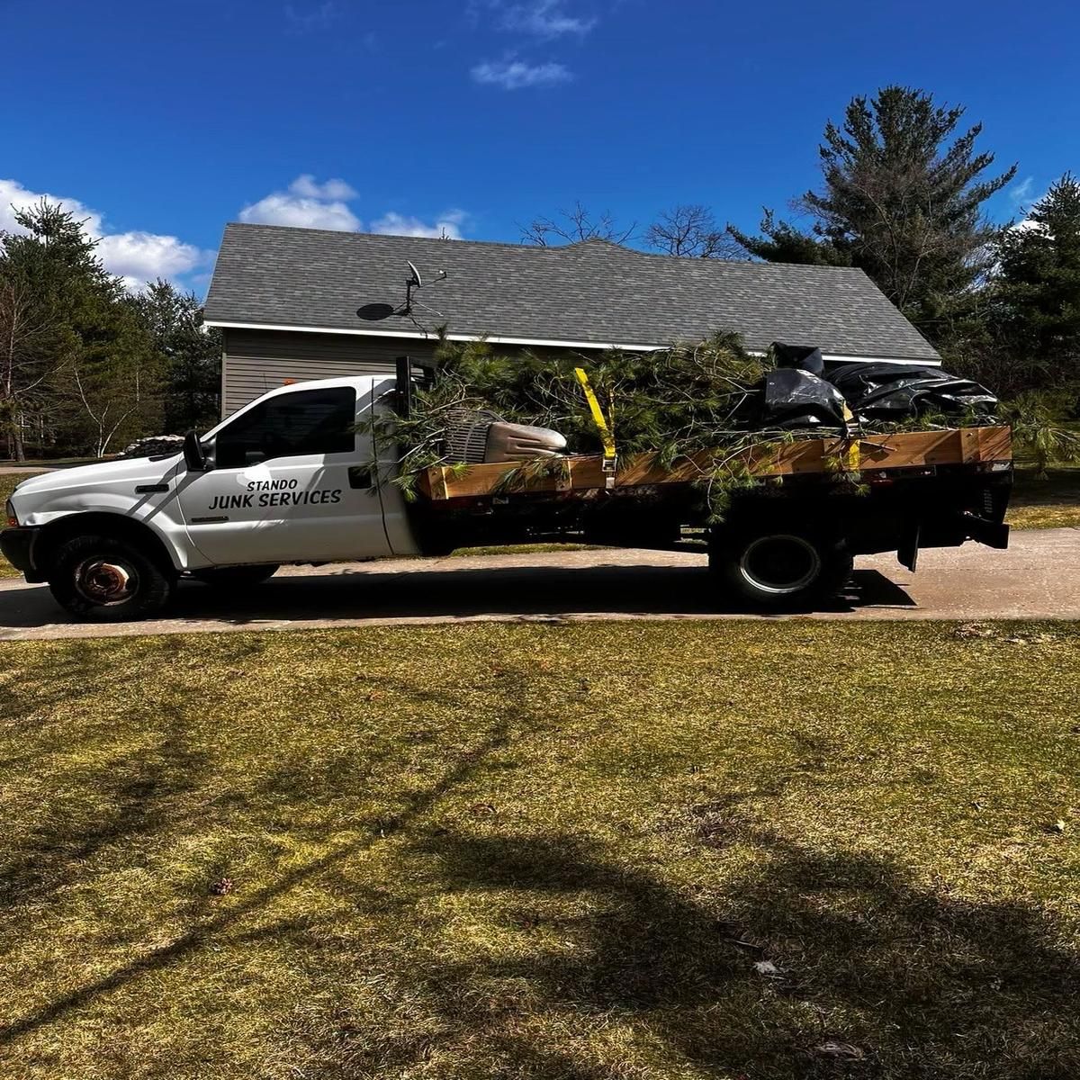 White utility truck loaded with potted plants parked in front of a house on a sunny day