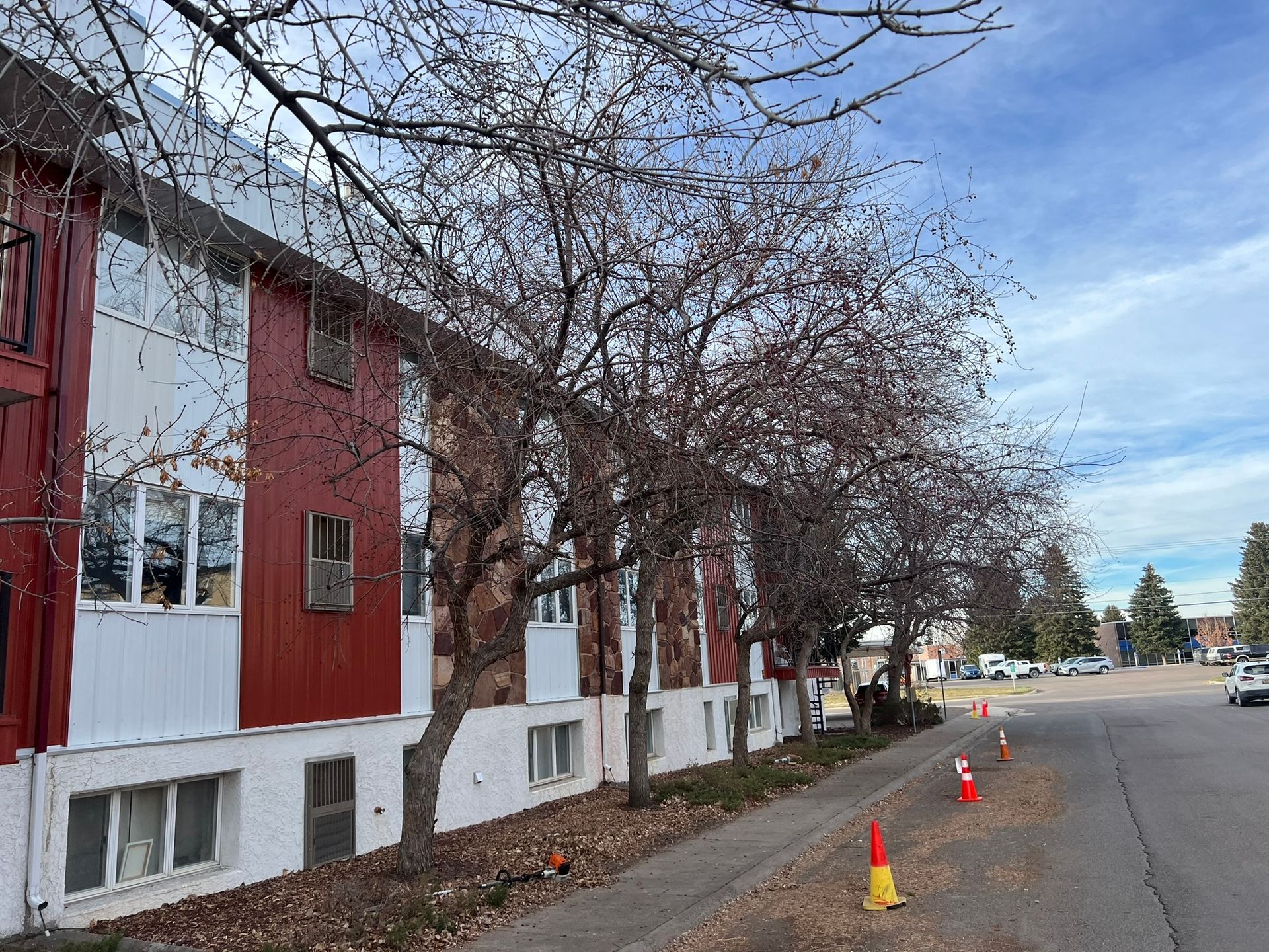 Red and white apartment building with bare trees along a street. Orange and white traffic cones are visible.