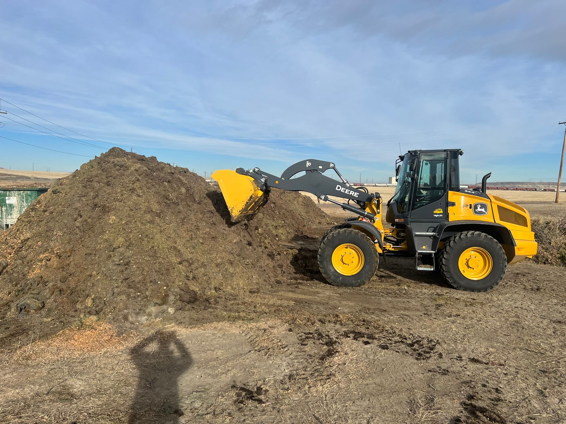 Yellow John Deere loader scoops compost on a sunny day.