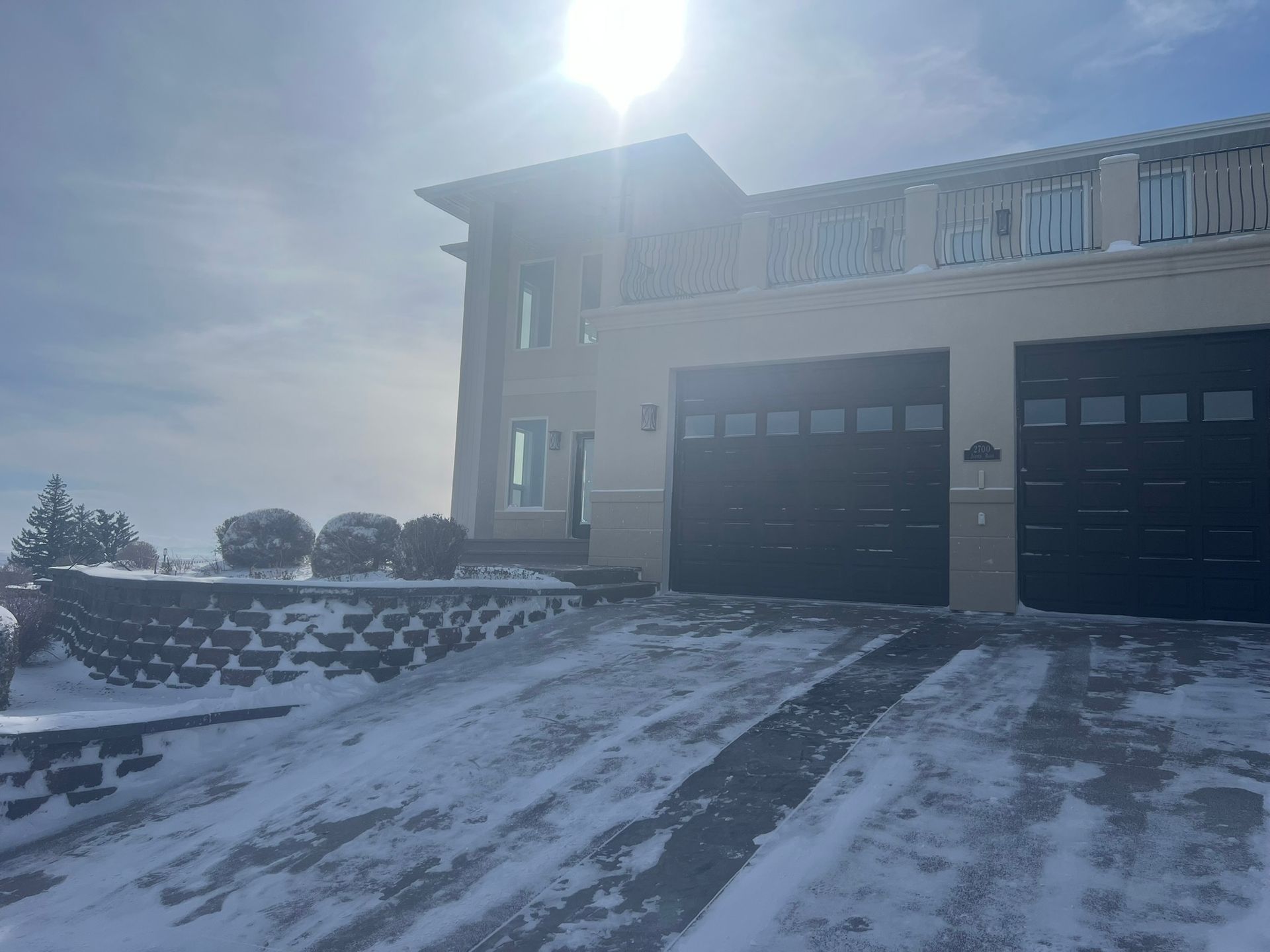 Snowy house exterior with dark garage doors, and a retaining wall.