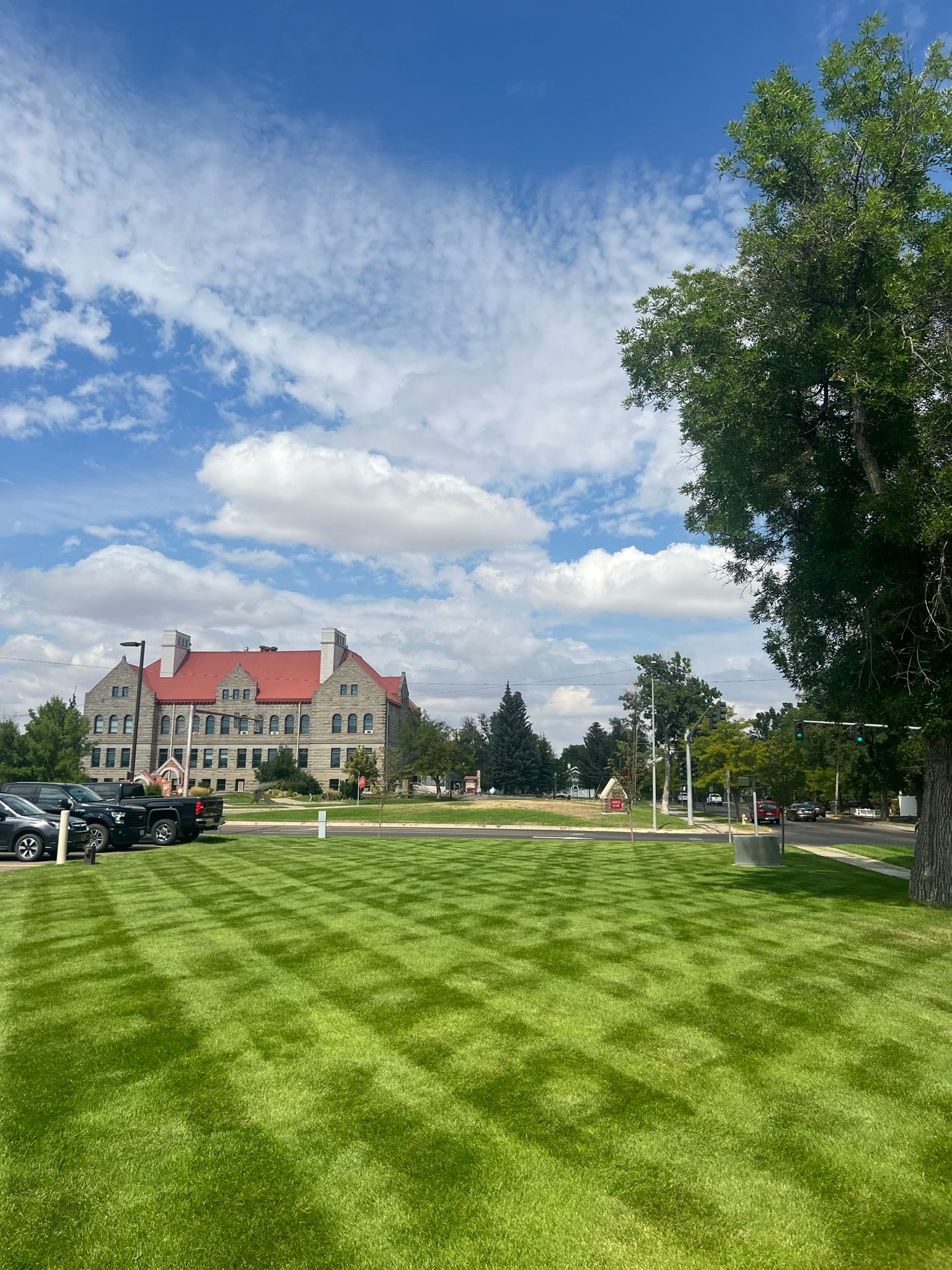 Lush green lawn with striped patterns, a grand stone building, and a bright blue sky with clouds.