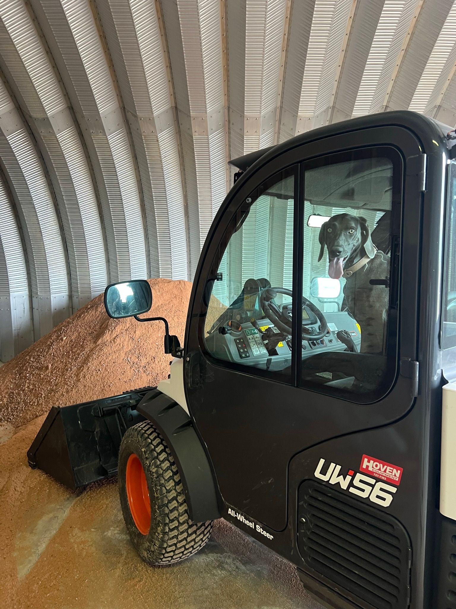 A black forklift with orange wheels, inside a building, next to a pile of brown material.