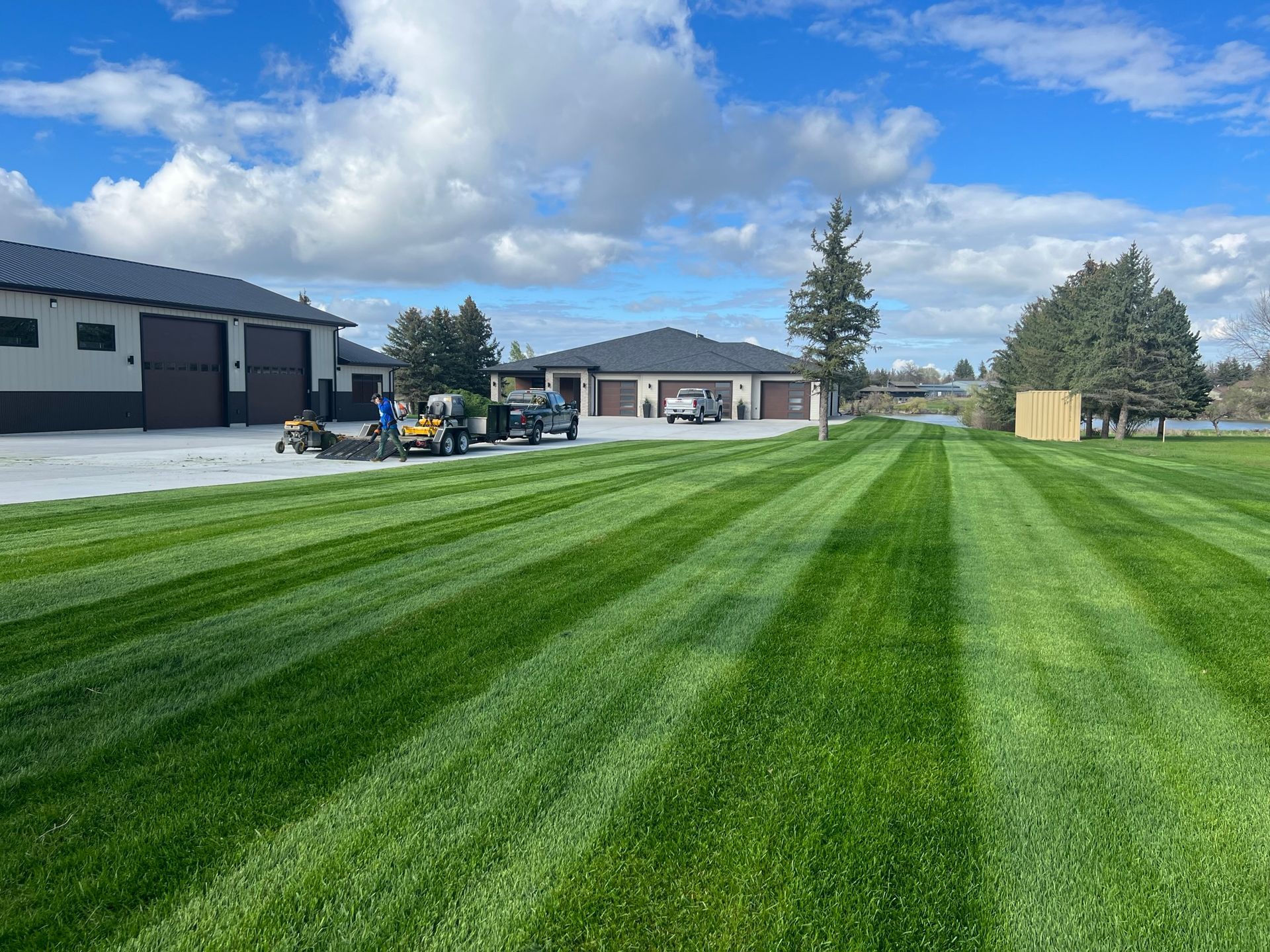 Lawn striped green and light, with buildings and equipment under a cloudy blue sky.