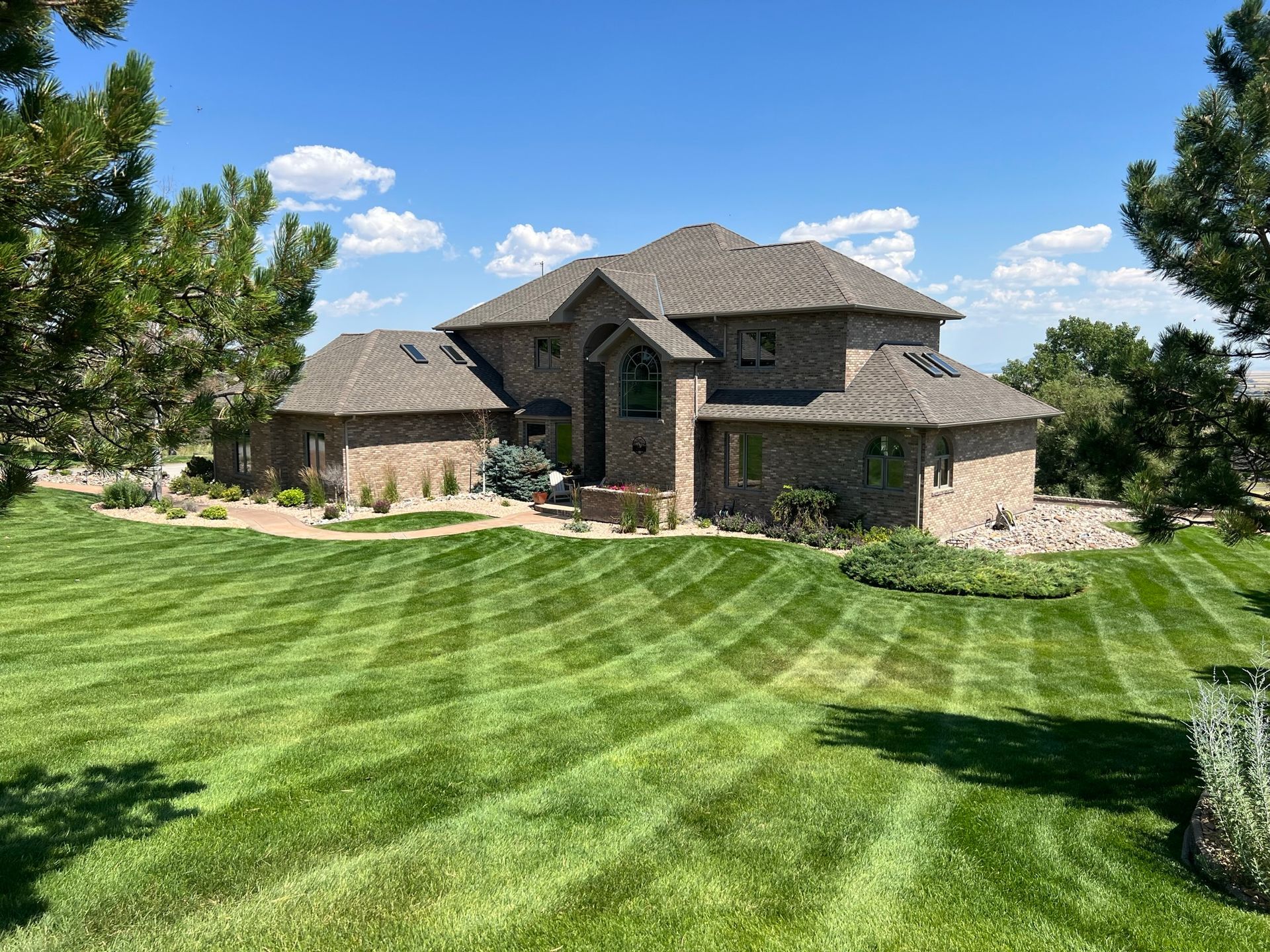Large brick house with patterned green lawn under a blue sky with clouds.