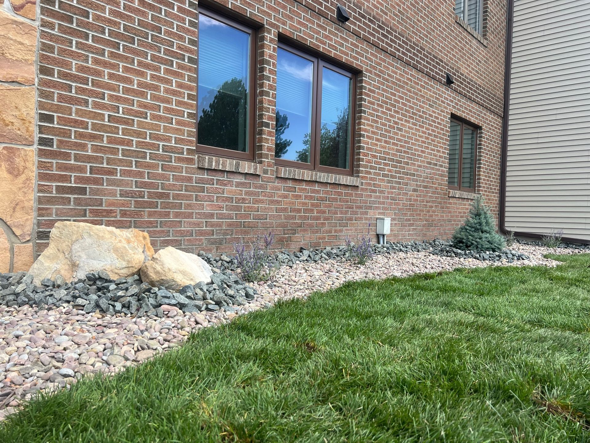 Brick building with windows, gravel and rock landscaping bordering green lawn.