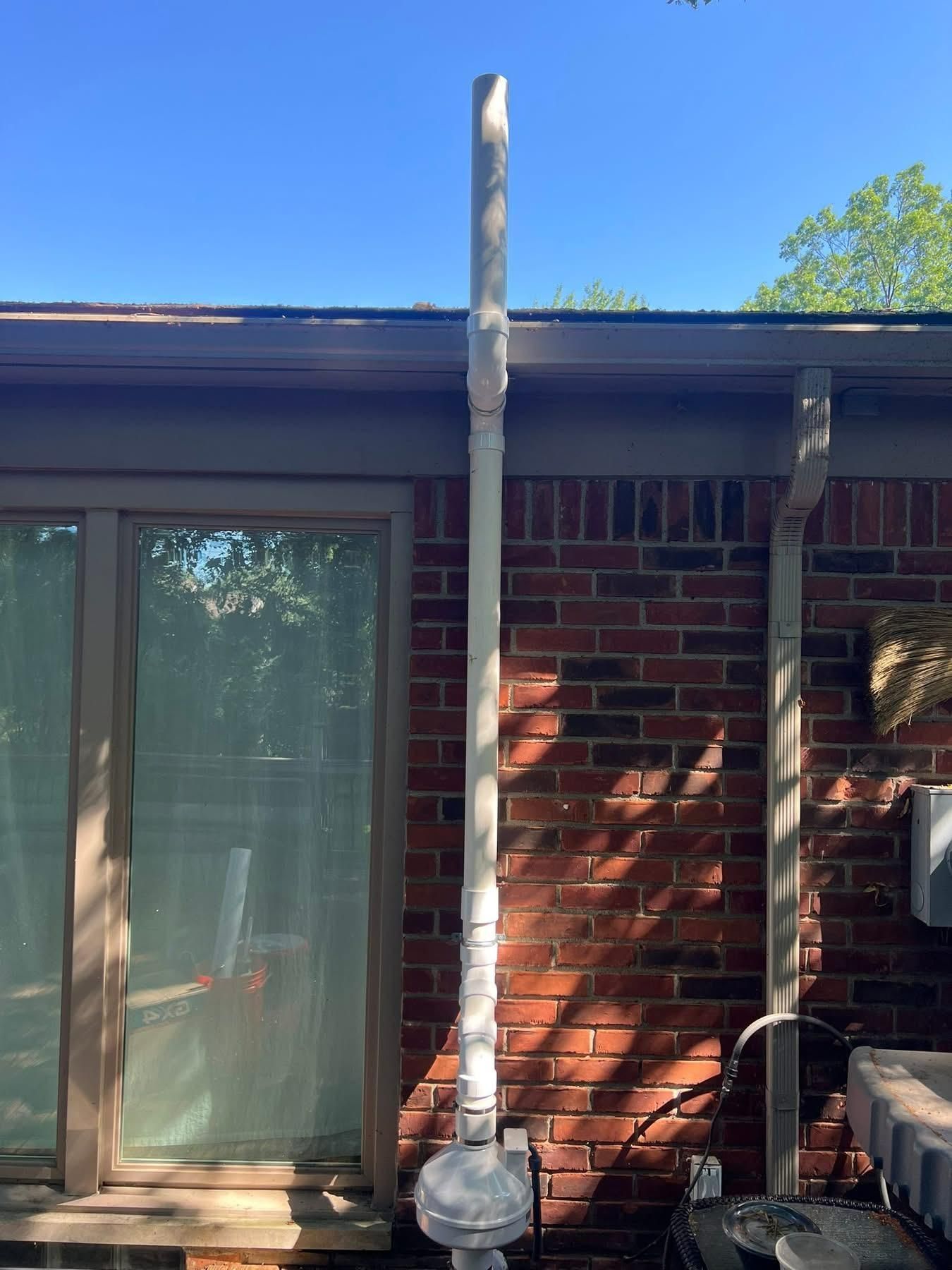 White PVC pipe extends vertically from a natural gas meter up the side of a brick building.
