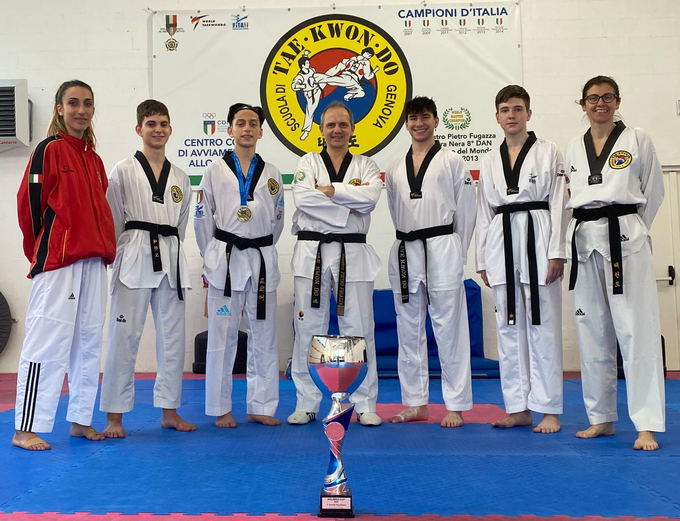 Una squadra di taekwondo in uniforme bianca posa con un trofeo in un dojo.