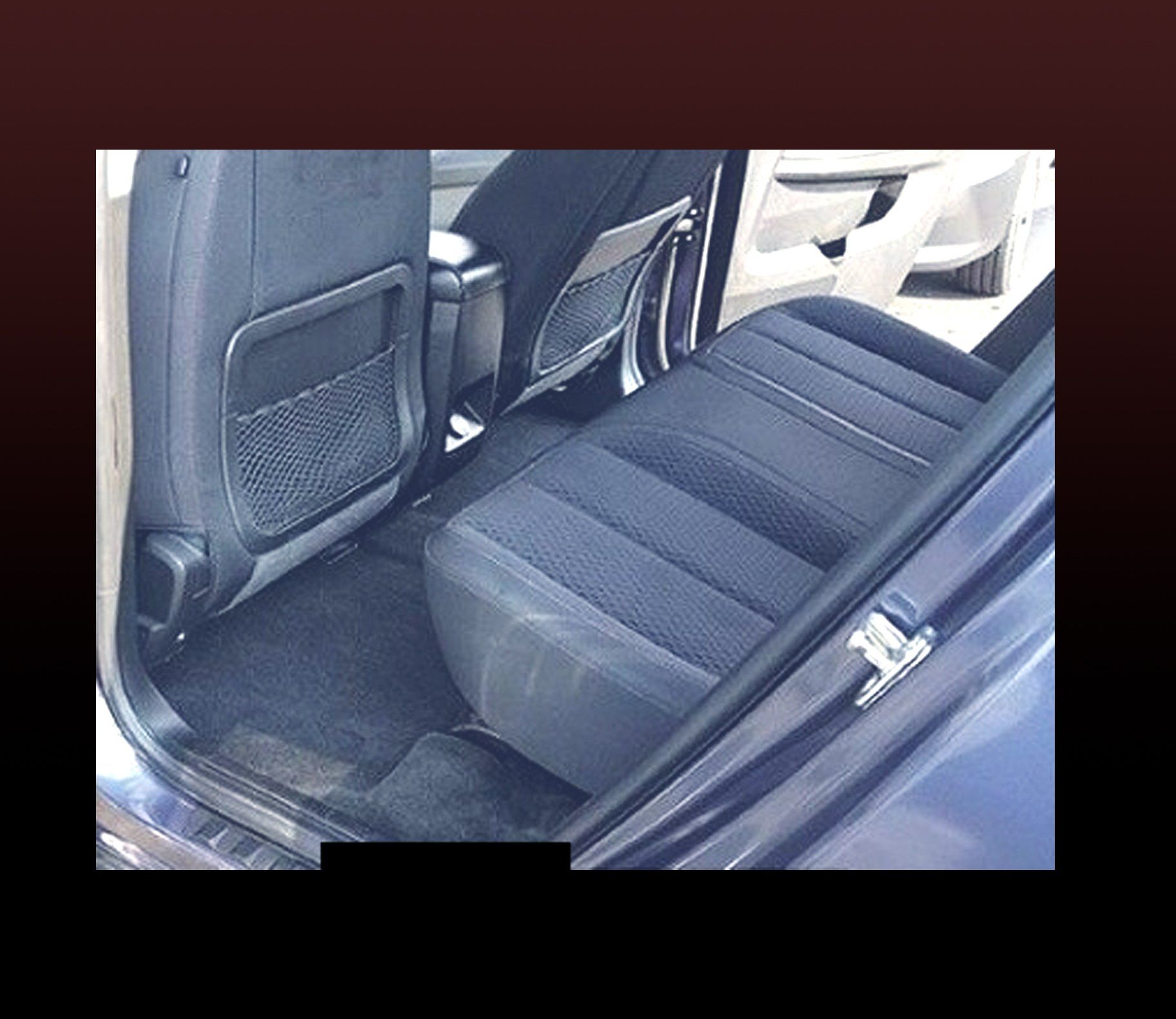 Rear interior car view: Black fabric seats with storage pockets, dark carpet.