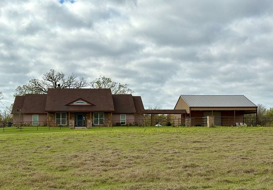 Rustic barn-style house with a red roof in a grassy field under cloudy skies