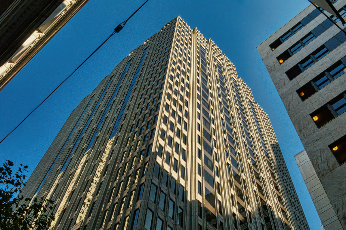 Tall skyscraper against a blue sky, viewed from below, with neighboring buildings at the edges.