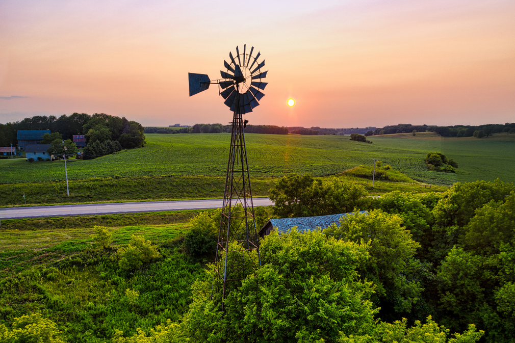 Windmill at sunset over green fields with a winding road and glowing orange sky