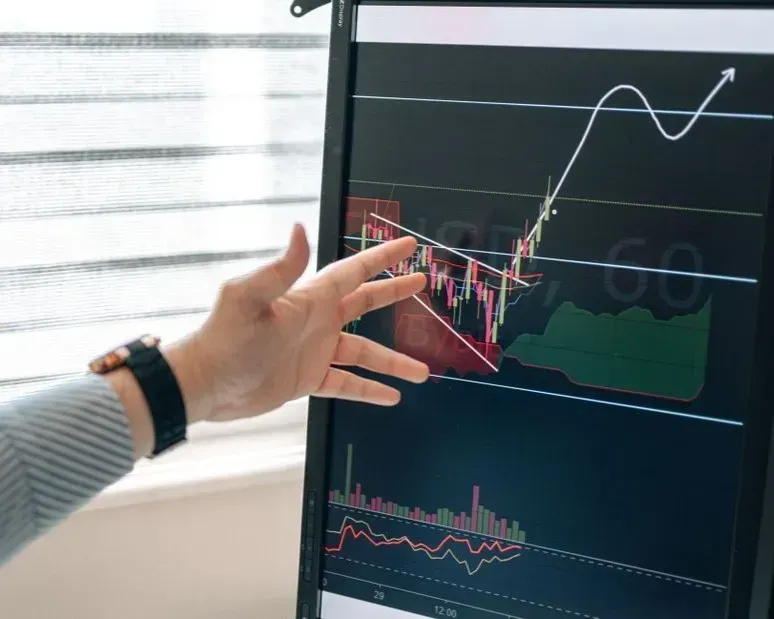 Hand pointing at a financial chart on a monitor with rising red and white graph lines