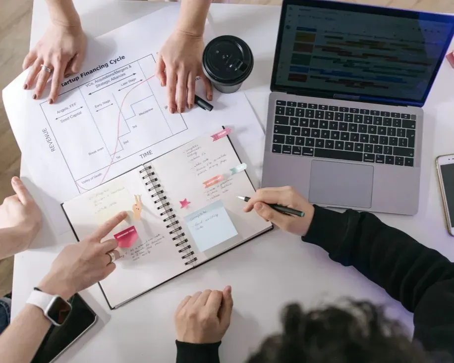 Hands reviewing charts and notes around a laptop in a collaborative meeting workspace
