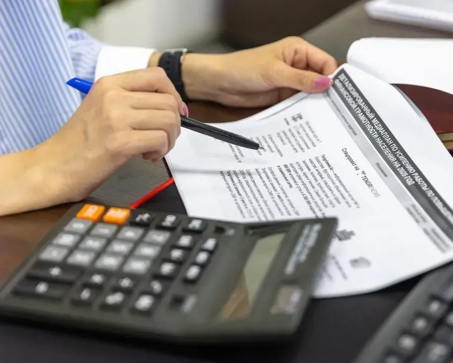 Hands holding a printed document beside a calculator on a desk