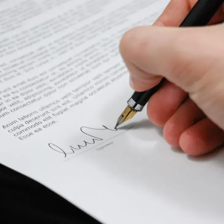 Hand signing a document with a black pen on white paper