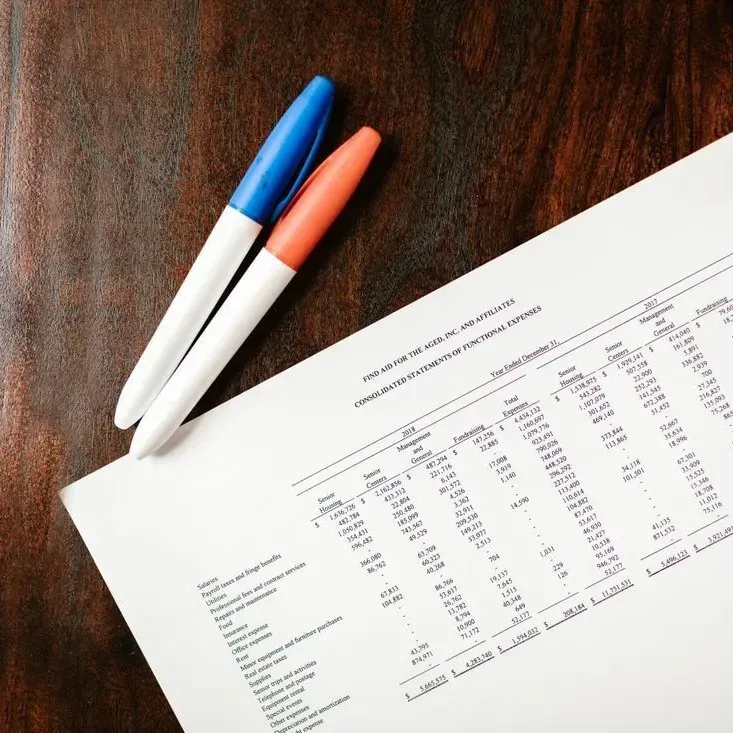 Two pens beside a printed financial report on a wooden desk