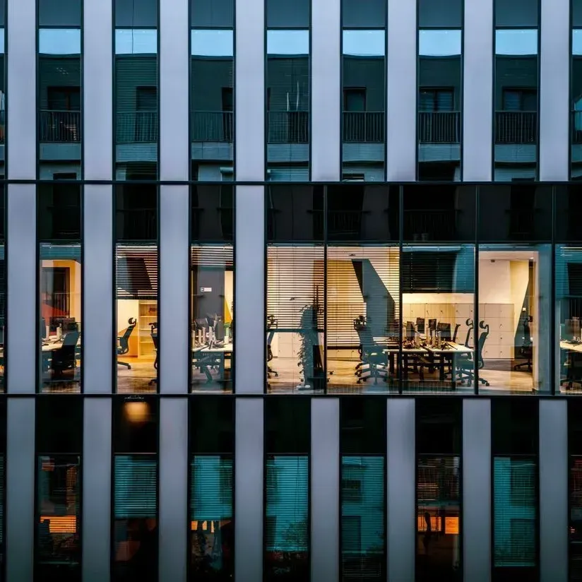 Office building facade with lit windows showing people working inside at dusk