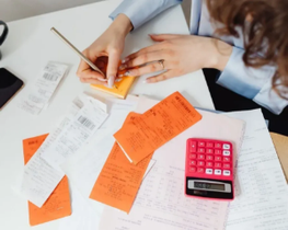 Hands writing on orange sticky notes beside scattered papers and a red calculator on a desk