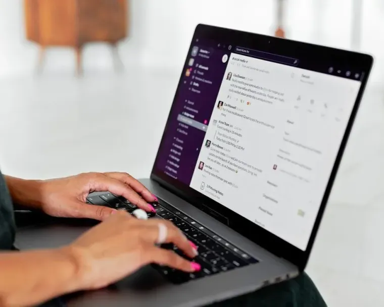 Hands typing on a laptop with a purple app interface on screen, in a bright indoor setting
