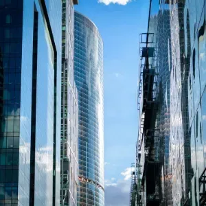 Modern glass office towers lining a narrow street under a blue sky